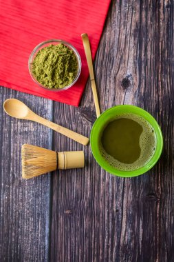 Kırmızı bir peçete ile ahşap bir yüzey üzerinde bir kase içinde maç yeşil çay. Üst görünüm, antioksidanlar, detoks içerir. Dikey yönlendirme