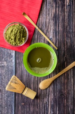 Kırmızı bir peçete ile ahşap bir yüzey üzerinde bir kase içinde maç yeşil çay. Üst görünüm, antioksidanlar, detoks içerir. Dikey yönlendirme