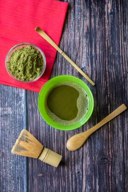 Kırmızı bir peçete ile ahşap bir yüzey üzerinde bir kase içinde maç yeşil çay. Üst görünüm, antioksidanlar, detoks içerir. Dikey yönlendirme