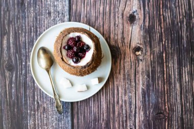 Ahşap bir arka plan üzerinde hindistan cevizi bir fincan yoğurt ile Berry tatlı. Böğürtlen, ahududu, yaban mersini, siyah kuş üzümü.