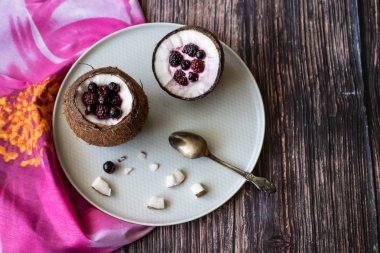 Ahşap bir arka plan üzerinde hindistan cevizi bir fincan yoğurt ile Berry tatlı. Böğürtlen, ahududu, yaban mersini, siyah kuş üzümü. Pembe peçete