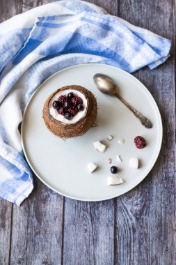 Ahşap bir arka plan üzerinde hindistan cevizi bir fincan yoğurt ile Berry tatlı. Böğürtlen, ahududu, yaban mersini, siyah kuş üzümü. Mavi peçete