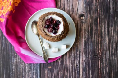 Ahşap bir arka plan üzerinde hindistan cevizi bir fincan yoğurt ile Berry tatlı. Böğürtlen, ahududu, yaban mersini, siyah kuş üzümü. Pembe peçete