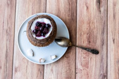 Ahşap bir arka plan üzerinde hindistan cevizi bir fincan yoğurt ile Berry tatlı. Böğürtlen, ahududu, yaban mersini, siyah kuş üzümü.