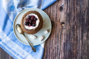 Ahşap bir arka plan üzerinde hindistan cevizi bir fincan yoğurt ile Berry tatlı. Böğürtlen, ahududu, yaban mersini, siyah kuş üzümü. Mavi peçete