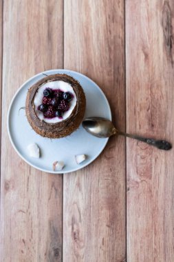 Ahşap bir arka plan üzerinde hindistan cevizi bir fincan yoğurt ile Berry tatlı. Böğürtlen, ahududu, yaban mersini, siyah kuş üzümü.