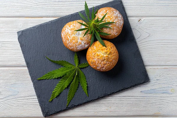 Cannabis muffins muffins muffins med kristaller CBD hampa blad, på svart krita och trä bakgrund Stockbild