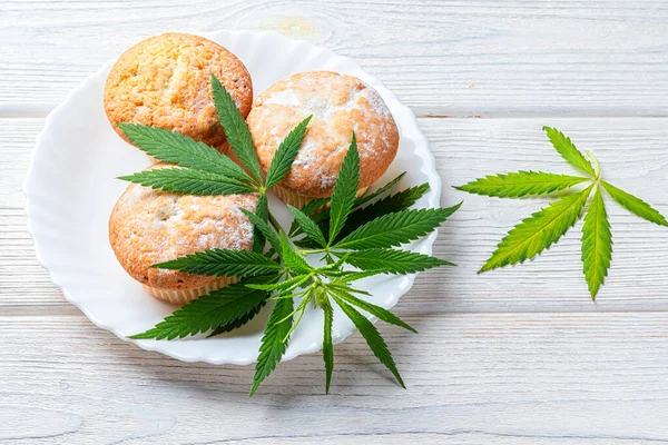 Cannabis muffins muffins med kristaller CBD hampa blad, på en vit platta och trä bakgrund Stockbild