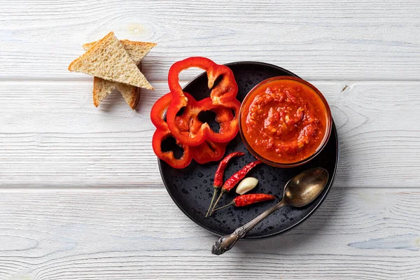 Ajvar eller pindjur röd grönsakssås, paprika peppar på en svart tallrik och träbord. Serbiska traditionella livsmedel Royaltyfria Stockfoton