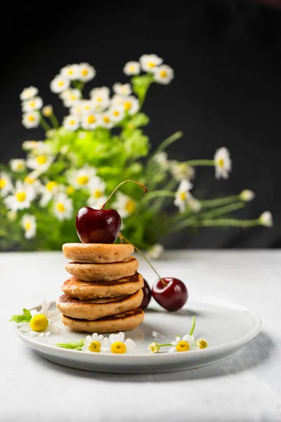Mini pannkakor med frukt och varenie på en tallrik med körsbär och kamomill i bakgrunden. Vertikal inriktning Stockbild