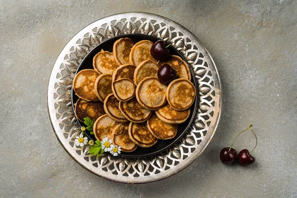 Um moderno café da manhã caseiro com mini panquecas e cerejas na mesa em um prato com aberturas. Orientação horizontal — Fotografia de Stock