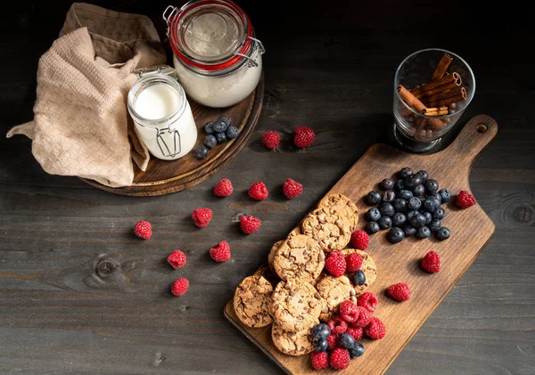 Tampo da mesa empilhados biscoitos de chocolate e bagas ao lado de paus de leite e canela — Fotografia de Stock