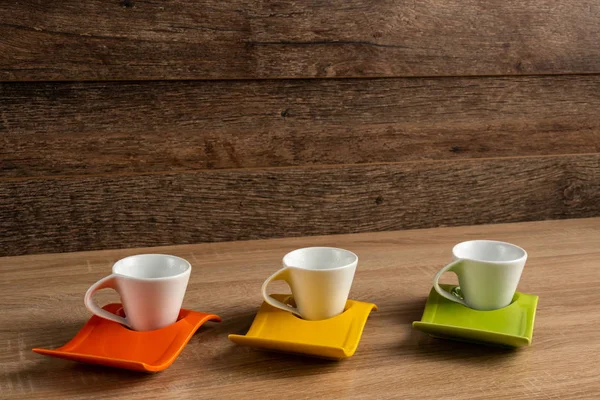 Side right to left inclined view of white coffee cups place on three colours plates.