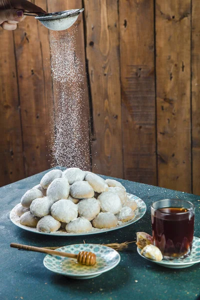 Female hand sprinkling powdered sugar over cookies