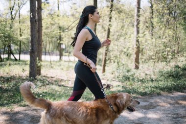 Parkta köpek gezdiren spor giysili bir kadın.