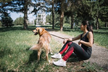 Park yolunda köpeğiyle oturan bir kız.