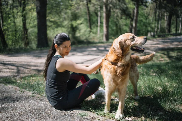 Genç bir kız köpeğiyle ormanda yerde oturuyor.