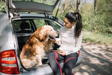 Doğada park edilmiş arabada oturan kız ve köpeğin portresi.