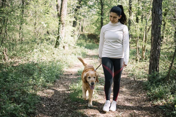 Spor kıyafetli bir kadın köpeğiyle yürüyor.
