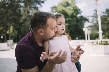 Baba küçük kızını kucaklıyor ve onunla konuşuyor.