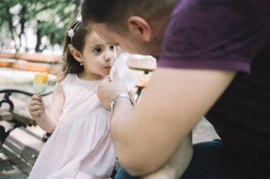 Baba dondurma yedikten sonra kızlarının yüzünü temizler.