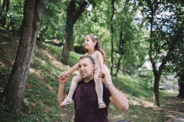 Parkta kızını omuzlarında taşıyan bir adam.