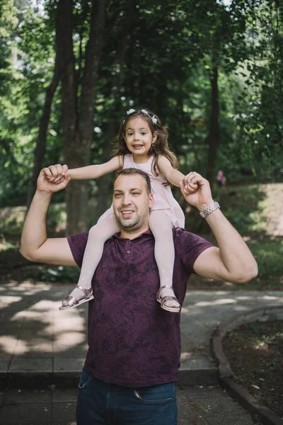 Man standing in park and holding child on shoulders