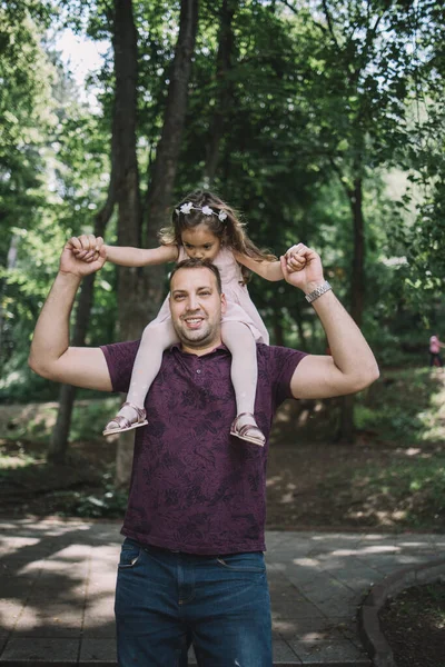 Yakışıklı baba ayakta duruyor ve kızını omuzlarına alıyor. — Stok fotoğraf