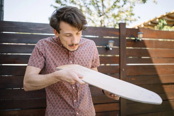 Muž foukání dřevo prach z leštěné skateboard palubě venkovní — Stock fotografie