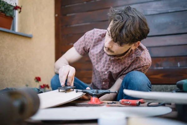 Man screwing skateboard part to wooden deck