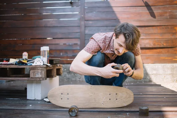 Glücklicher Mann hält Rad, während er Skateboard-Teile montiert — Stockfoto