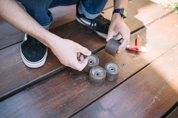 Male hands taking skateboard wheel from wooden surface