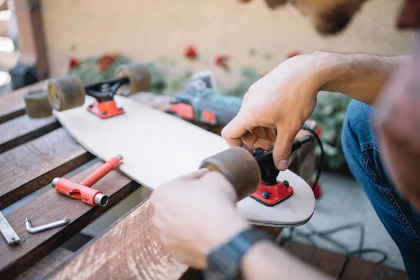 Cropped man screwing skateboard wheel to board in backyard — Stock Photo, Image