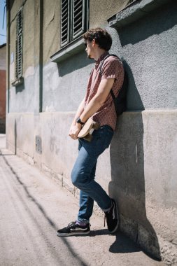Duvara yaslanan ve kaykayı tutan adam