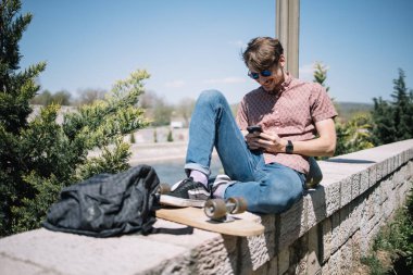 Güneş gözlüklü gülümseyen adam dışarıda telefon kullanıyor.