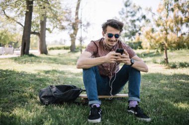 Parkta otururken müzik dinleyen yakışıklı adam.