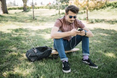 Ormanda müzik dinleyen güneş gözlüklü çekici bir adam.