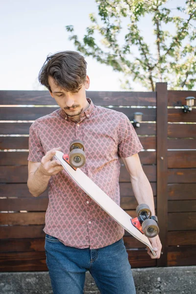 Bearded man holding skateboard while standing outdoor