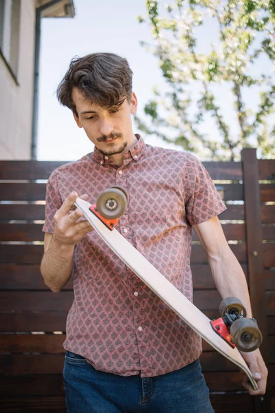 Muž kontroluje skateboard kola, zatímco stojí na dvoře — Stock fotografie