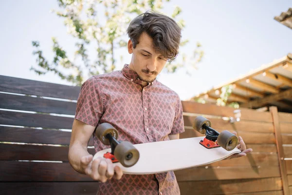 Brunette man holding skateboard and checking wheels