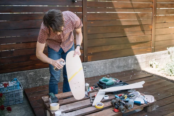 Brünetter Mann steht im Hof und bemalt Skateboard — Stockfoto