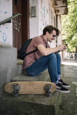 Gülümseyen adam merdivenlerde oturuyor ve cep telefonu kullanıyor.