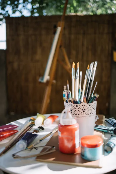 Mesa branca com acessórios de pintura colocados no jardim — Fotografia de Stock