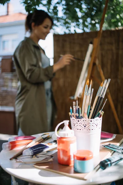 Mesa con tubos de pintura y pinceles delante del artista desenfocado — Foto de Stock