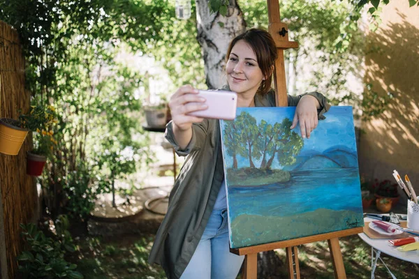 Jovem mulher tirando foto de si mesma enquanto posando ao lado da pintura — Fotografia de Stock