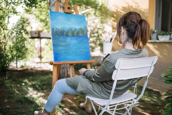 Visão traseira da mulher sentada na cadeira e olhando para tela pintada — Fotografia de Stock