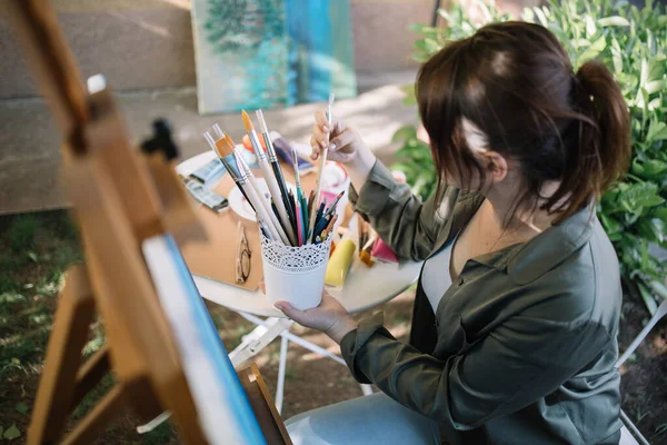 Morena mulher segurando pote com pincéis de pintura ao ar livre — Fotografia de Stock