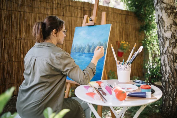 Kvinna konstnär målning bild i utomhus studio Stockbild