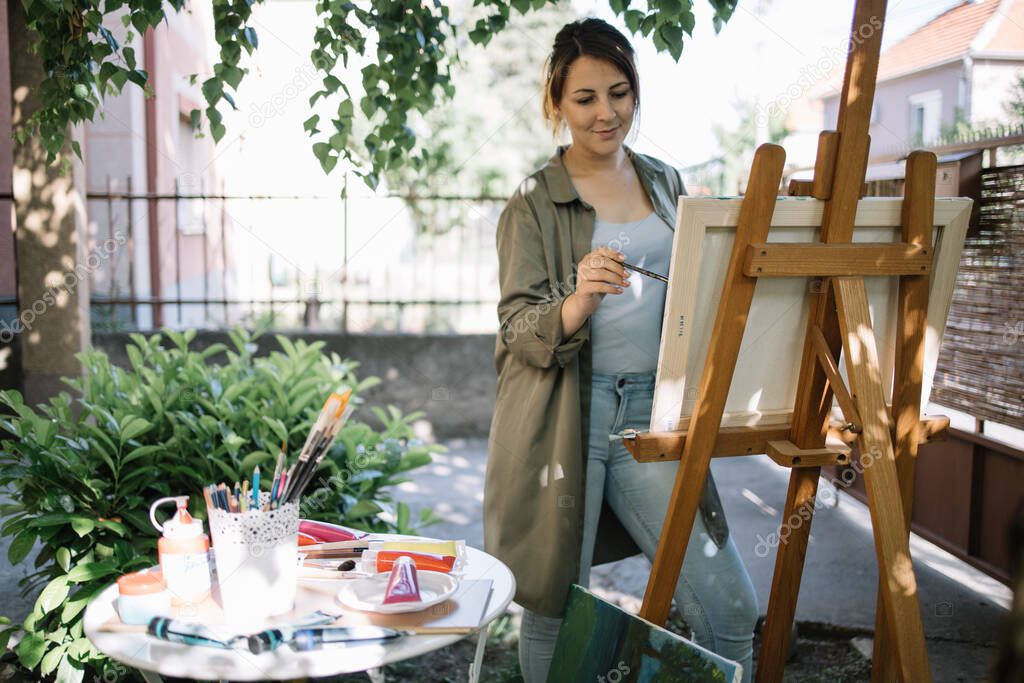 Female artist using paint brush while painting in backyard