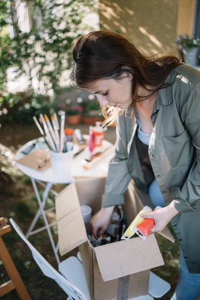 Mujer joven recogiendo tubos de pintura de la caja — Foto de Stock